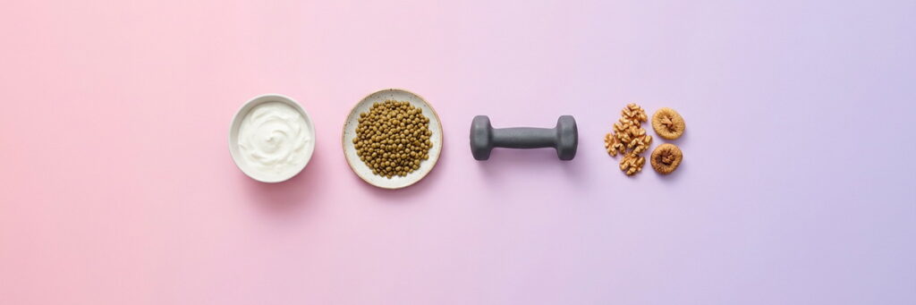 Alta proteína y microbiota: qué cambia con el entrenamiento de fuerza 4 Yogur, lentejas, una mancuerna y frutos secos en fila sobre un degradado pastel rosa y lavanda