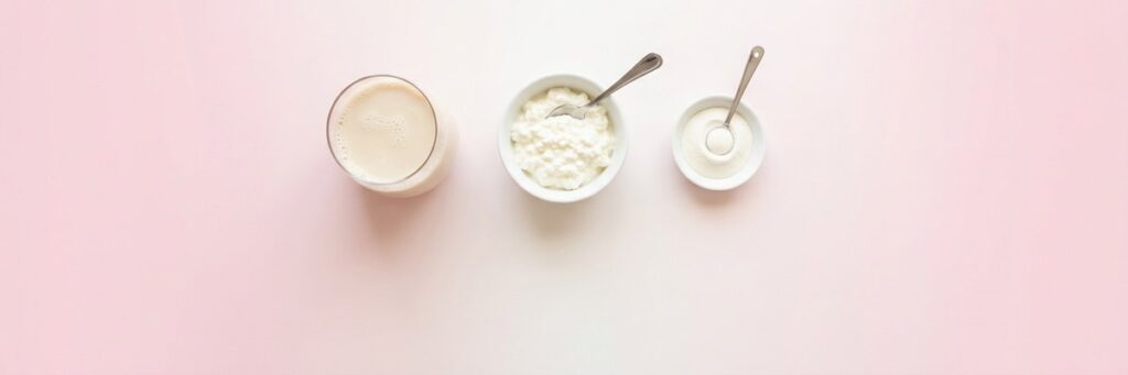 Aminoácidos libres o proteína entera: qué conviene en cada caso 7 Vaso de leche, cuenco de requesón con cuchara y cuenco de yogur sobre un degradado pastel rosa