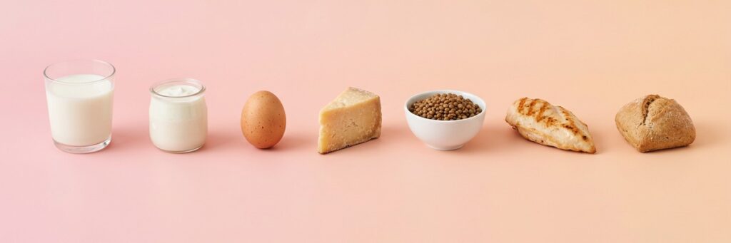 Niño selectivo con la comida: cómo sumar proteína sin peleas 2 Fila de alimentos ricos en proteína sobre fondo pastel: leche, yogur, huevo, queso, lentejas, pollo y pan